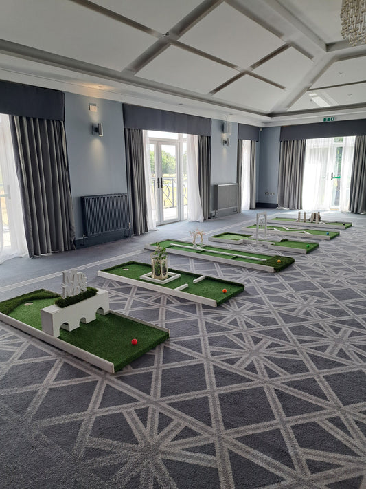 An indoor 6 hole wedding golf course set up in a large function room with a grey geometric patterned carpet. Formby Hall & Spa Golf resort, Formby.