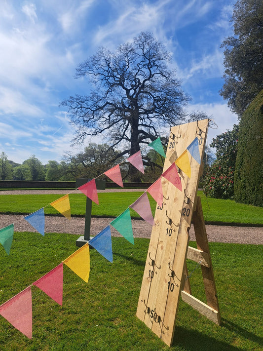 Wooden target with hooks on and colourful flags on a grassy area under a blue sky.