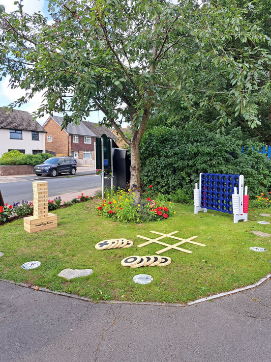 3 garden games - giant versions of jenga, connect 4 & noughts & crosses - set up on a grassy lawn under a tree and houses in the background