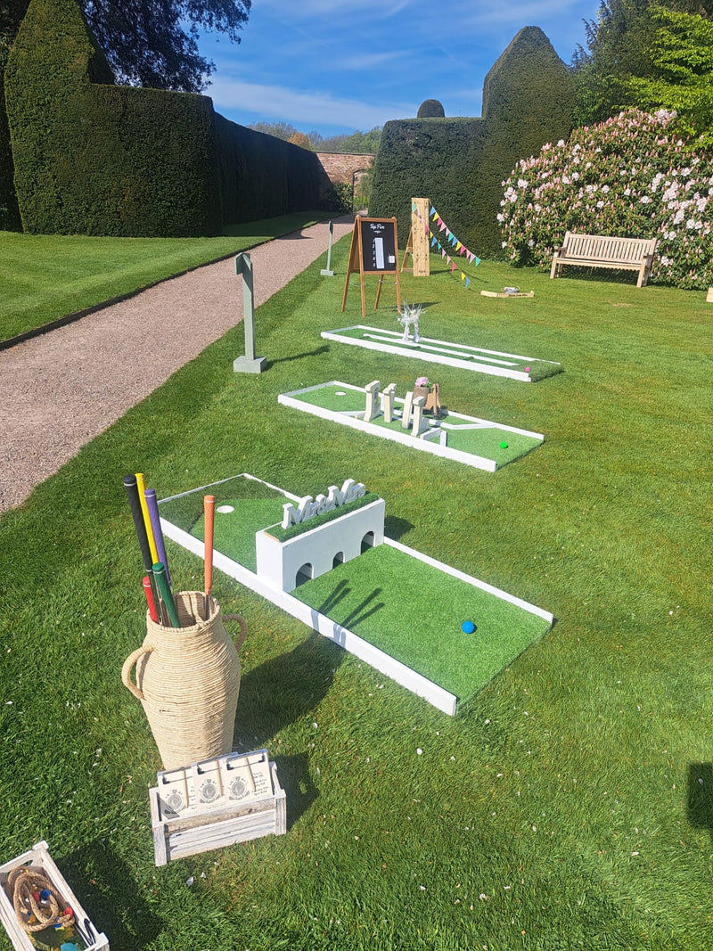 Miniature golf course setup on a grassy area with a bench and trees in the background.