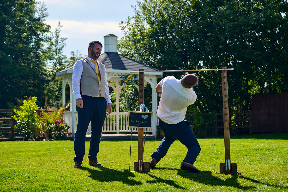 Two wedding guests outdoors on a grassy lawn in front of a white gazebo playing Limbo at The Aviary, Ormskirk