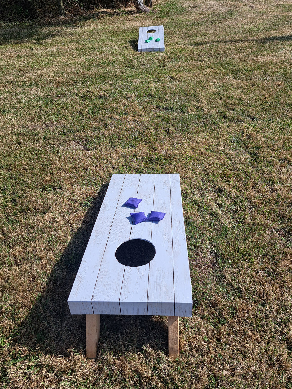 A white wooden cornhole board, set on a grassy lawn outdoors. A second cornhole board is visible in the background. Wedding at a private residence, Fylde coast.