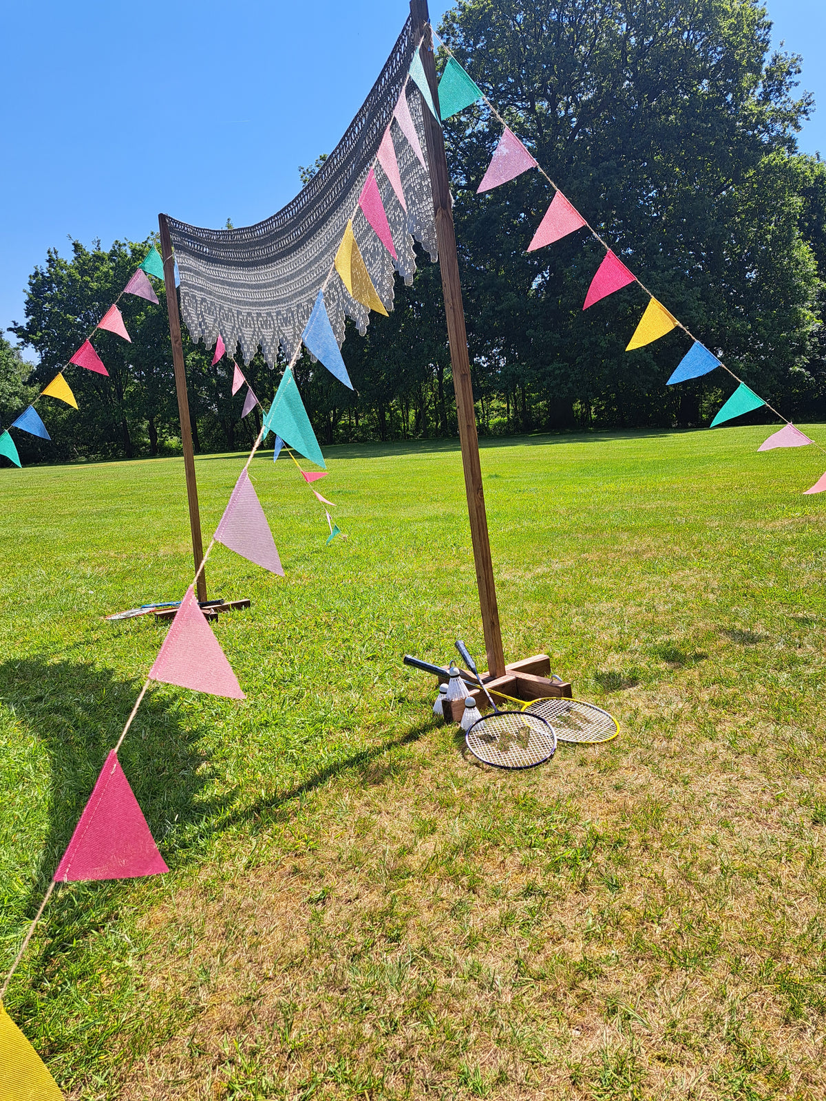 A badminton court with colourful triangular flags on a string against a blue sky with a grassy field below. Bartle Hall, Preston