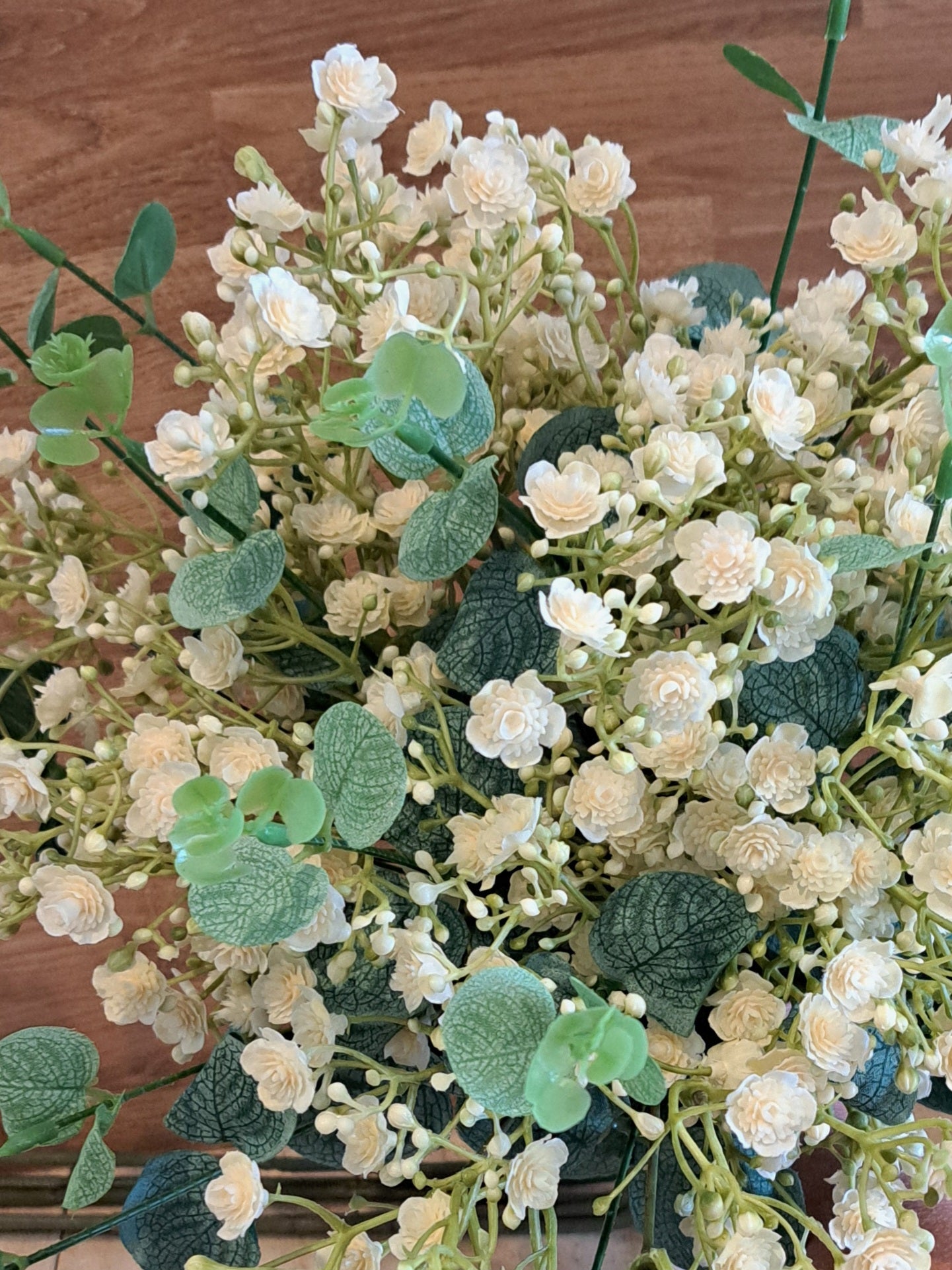 A close up image of bridal bouquet of  ivory gypsophila and green eucalyptus leaves against a wooden background.