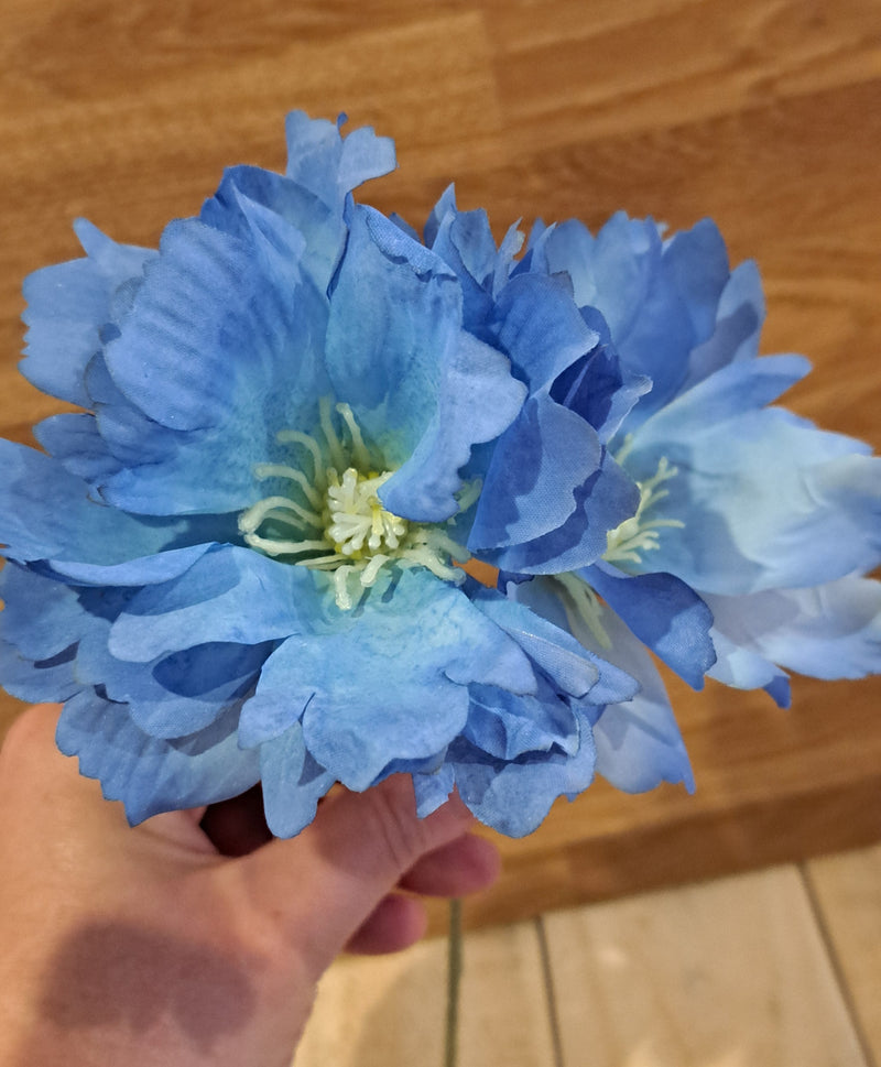 Artificial blue delphiniums with white centre, held in a hand with a wooden background