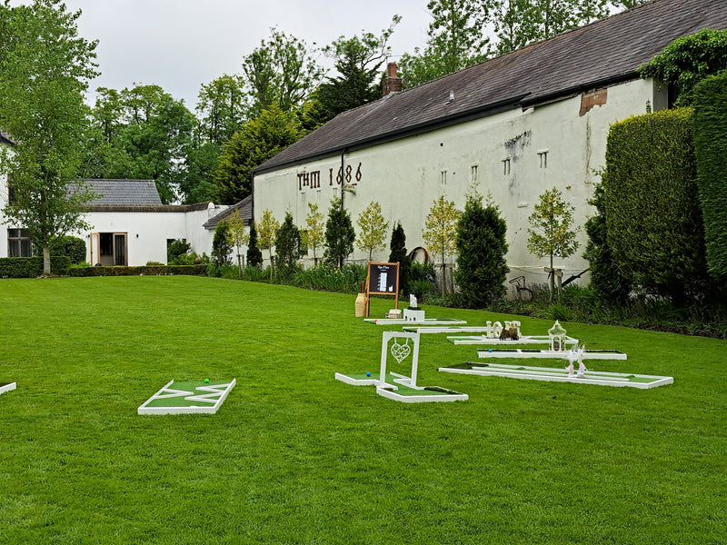 A miniature wedding golf course set out on a grassy lawn and white buildings in the background