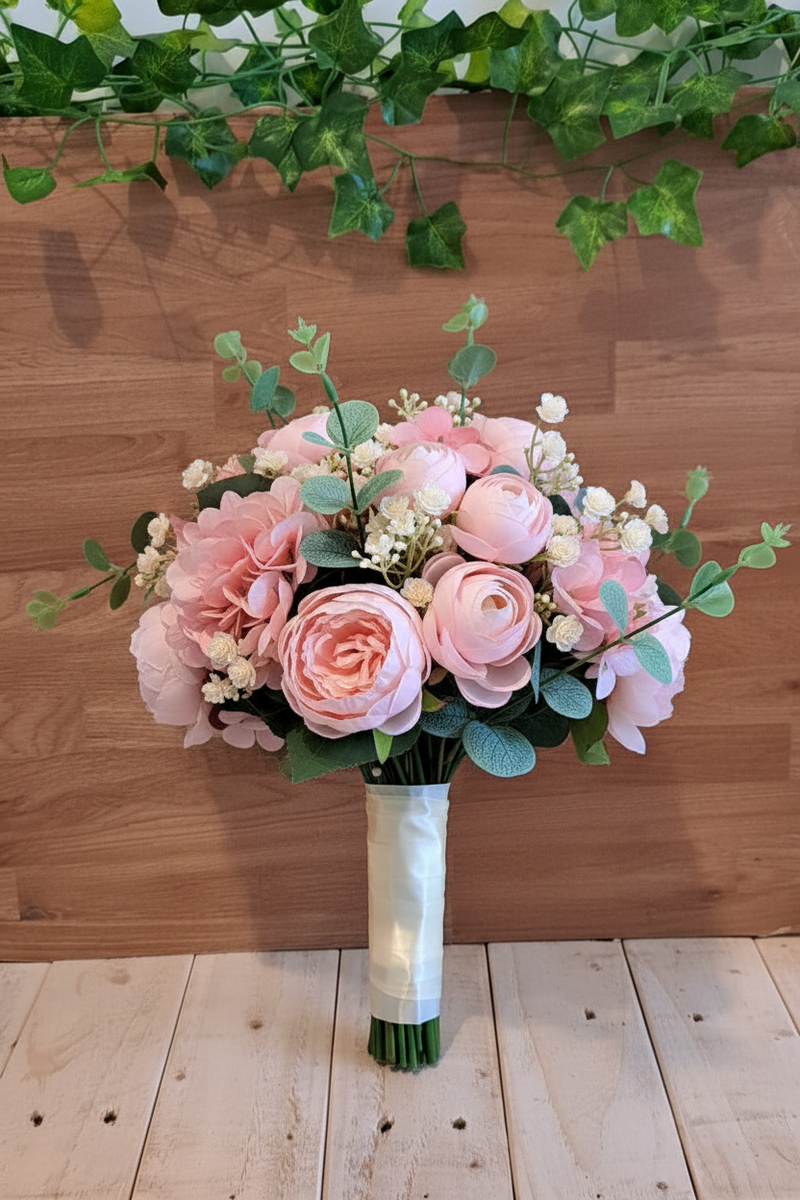 A small bouquet of pink peonies, hydrangea, gypsophila and eucalyptus, tied with a white ribbon on a rustic wood shelf