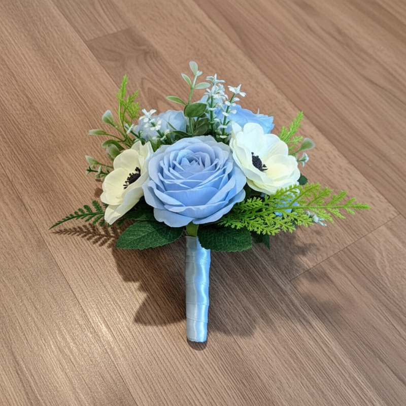 A bridesmaid bouquet of white anemones and pale blue roses with foliage, wrapped in a blue ribbon