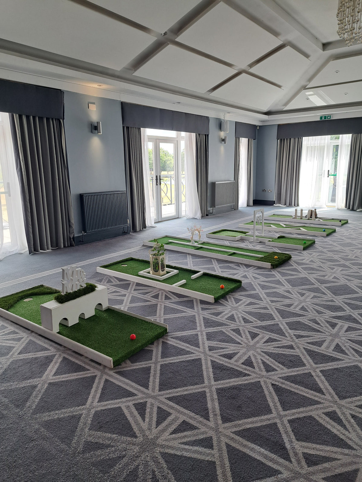 An indoor 6 hole wedding golf course set up in a large function room with a grey geometric patterned carpet. Formby Hall & Spa Golf resort, Formby.