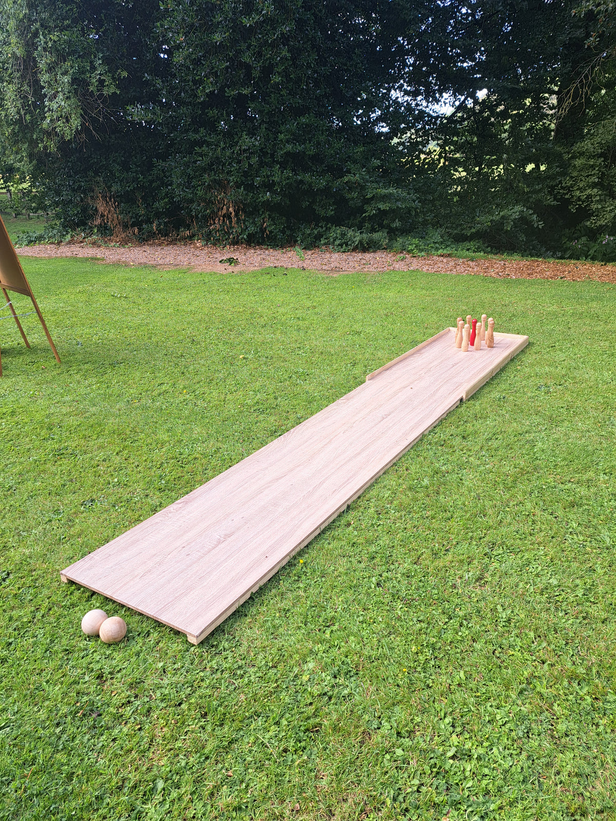 An outdoor wooden lawn bowling game set on a green grass lawn, with a long wooden lane, bowling pins, and two bowling balls. Private garden for a wedding near Blackpool.