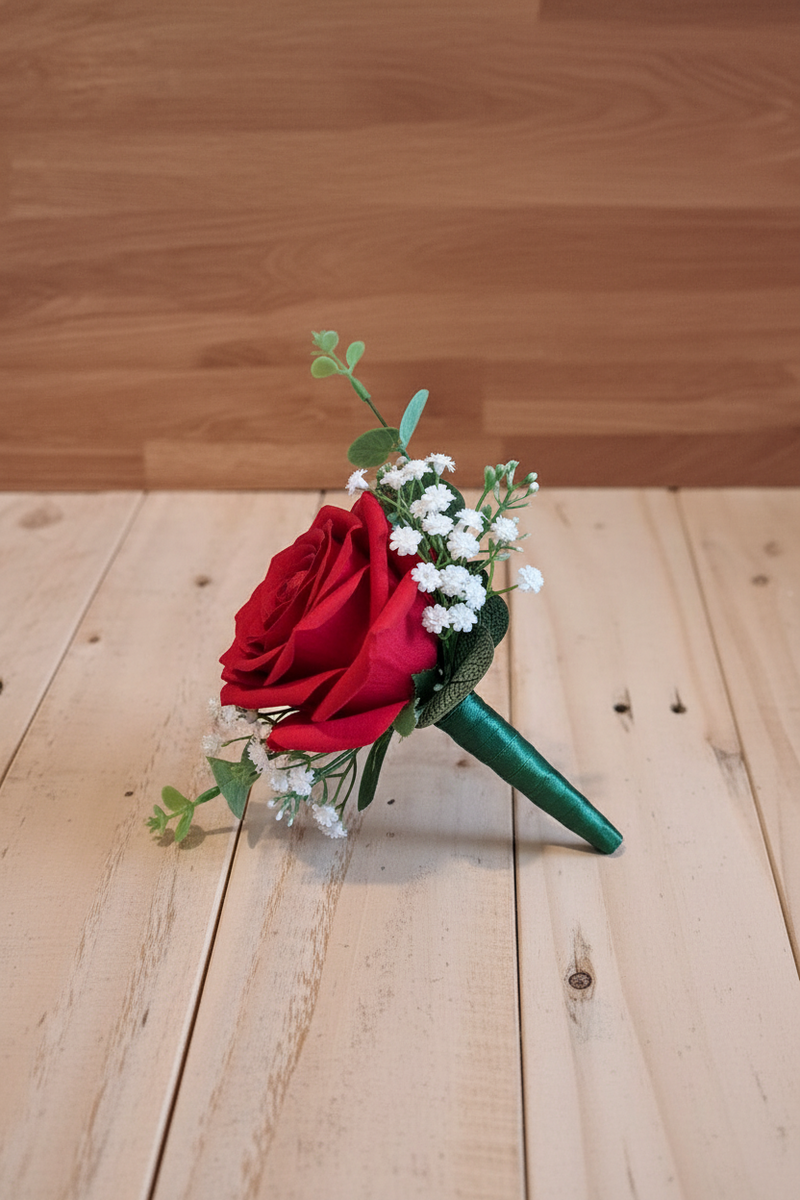 A grooms button hole with one red rose and baby breath tied with a green ribbon