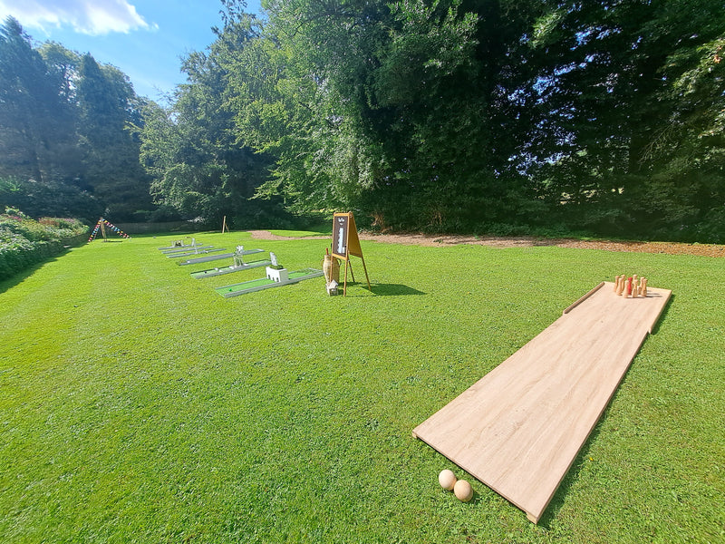 6 hole wedding mini golf course and a 9 pin bowling alley set up for a wedding on a grassy lawn, surrounded by trees under a blue sky. Mitton Hall, Clitheroe.