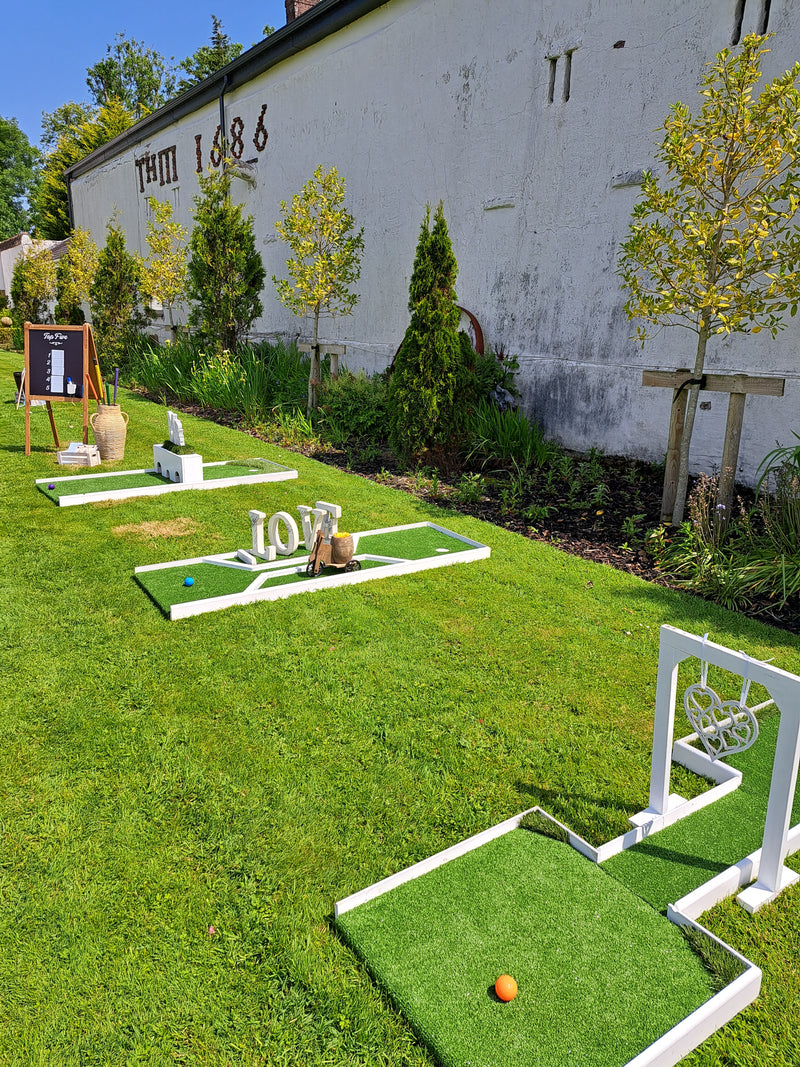 Miniature golf course with green grass and white decorative on a lawn in front of a white building